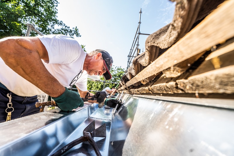 Roof worker fitting a gutter at the roof edge