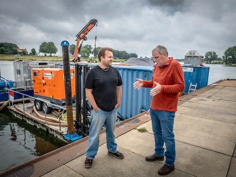 Gemeentelijk archeoloog Johan van Kampen (links) en amateur-archeoloog/duiker Joost van den Besselaar staan op de loswal van Cuijk. Achter hen het ponton dat de komende maanden dienst doet als werkeiland bij opgravingen van Romeinse resten die in de bodem van de Maas zitten. 