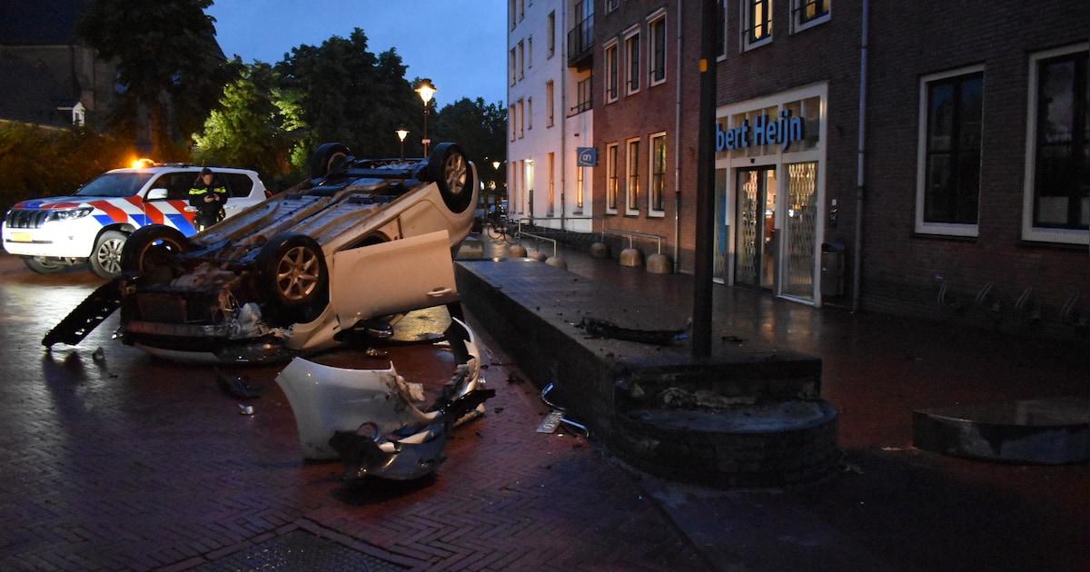 Auto op de kop na botsing met stenen rand voor supermarkt in Bemmel