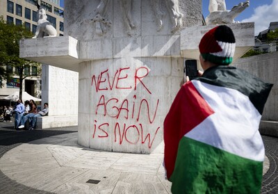 Betoger spuit leus op Nationaal Monument op de Dam tijdens demonstratie
