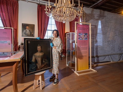 Jacoline Zilverschoon, directeur van het Flipje en Streekmuseum, in de Stijlkamer. Ze houdt het portret vast van Margaretha van Vijgh, op de achtergrond hangt het portret van Jacob Willem van Eck. Rechts het doek dat deel uitmaakt van het project Draden van ons Nederlandse Slavernijverleden.